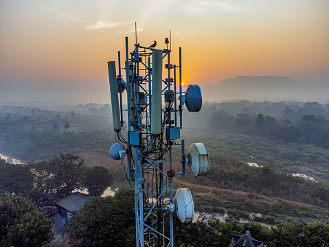 Telecommunication equipment and antenna mounted on a cell tower in a remote rural area with a backdrop of sunrise over the hills.
